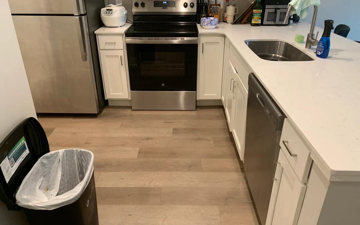 Client-supplied kitchen photo showing clear flooring, white cabinets, and stainless appliances.
