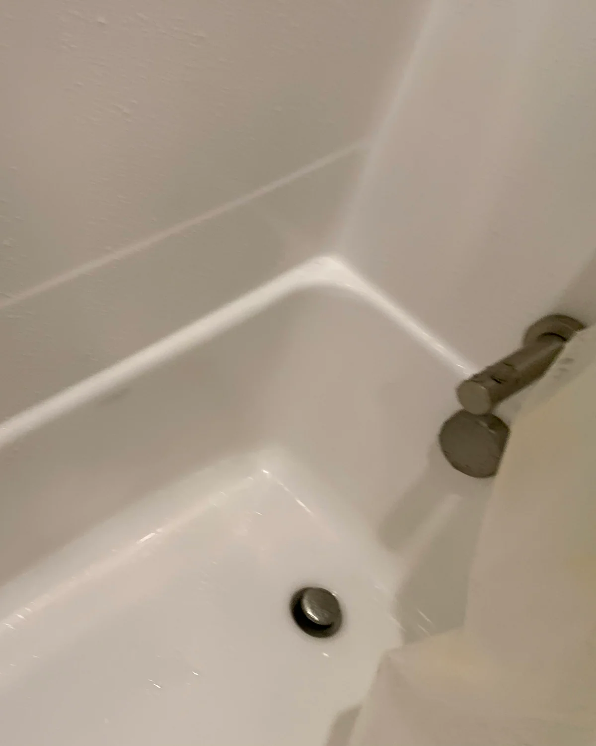 Client-supplied photo of a white bathtub with a clear surface around the drain.