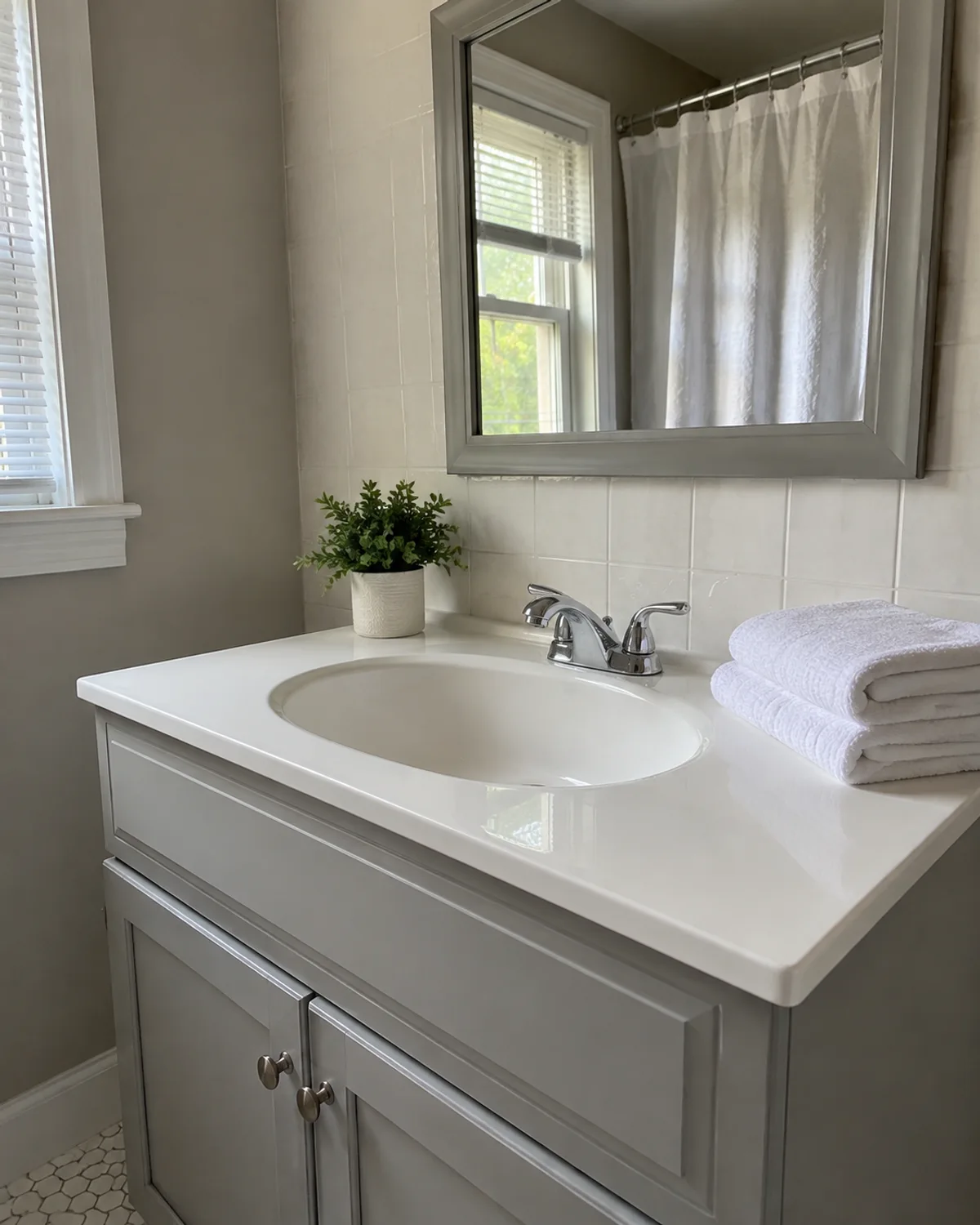 Clean white bathroom sink and chrome faucet above a gray vanity, with folded towels and a framed mirror.